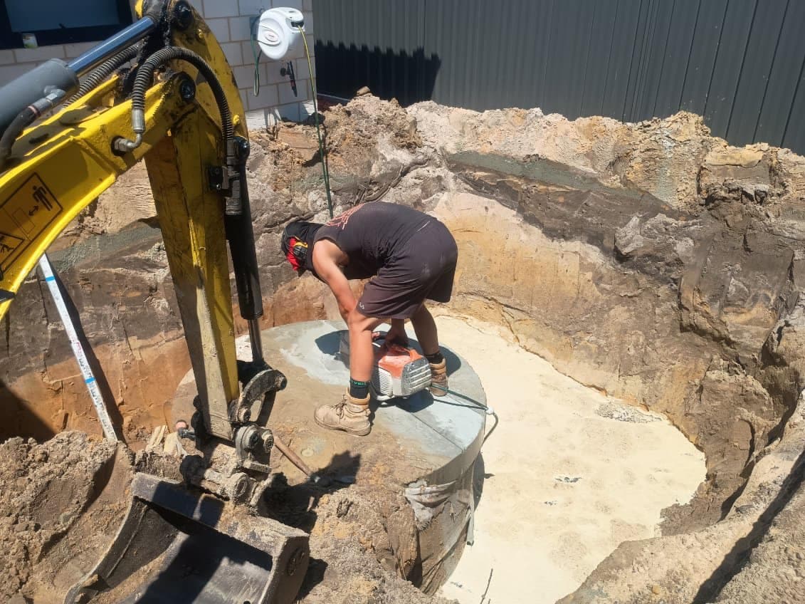 Tradesman grinding concrete inside a pool excavation